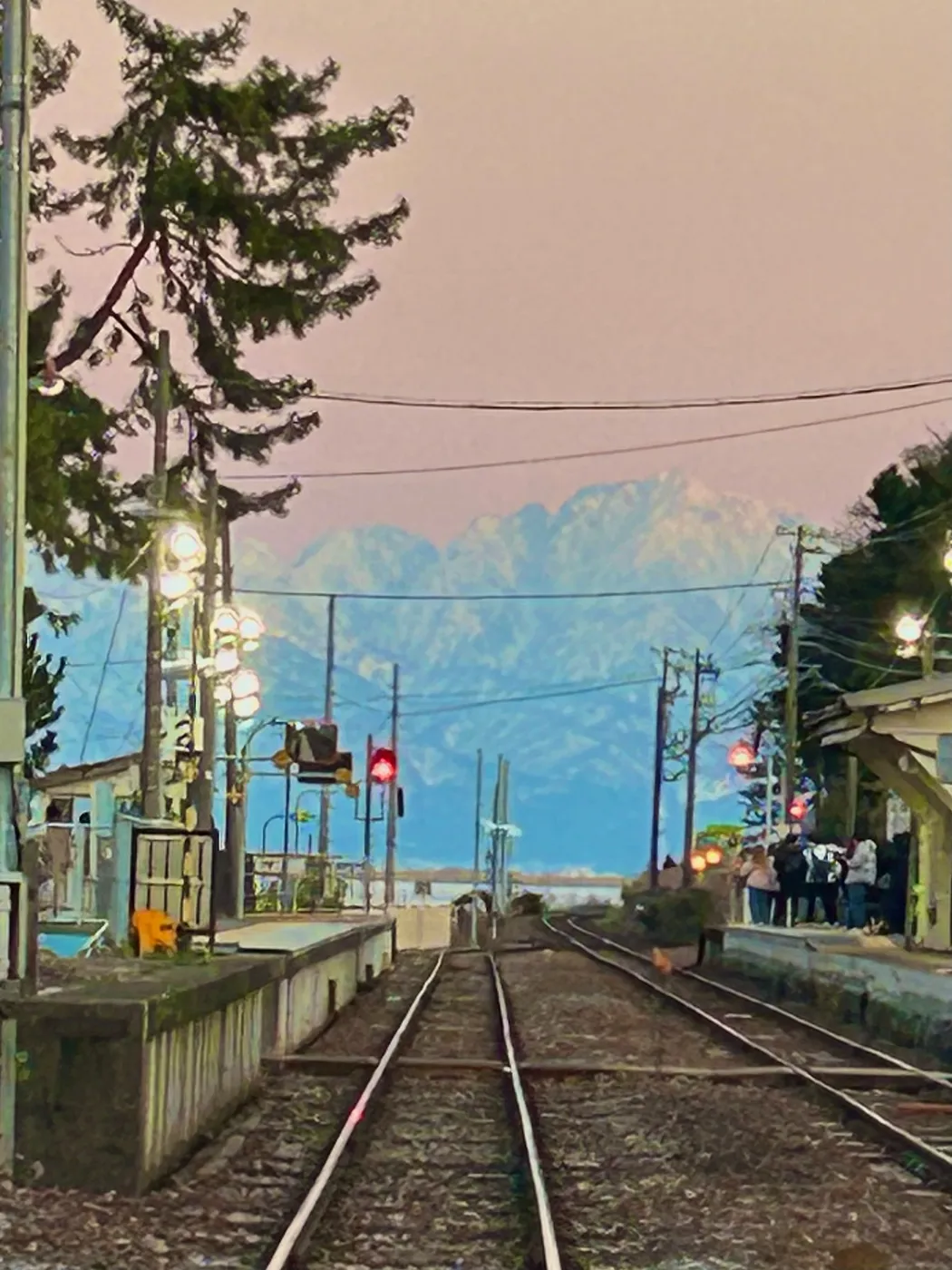 The platform and tracks of Amaharashi Station at dusk, with the Tateyama mountains beyond